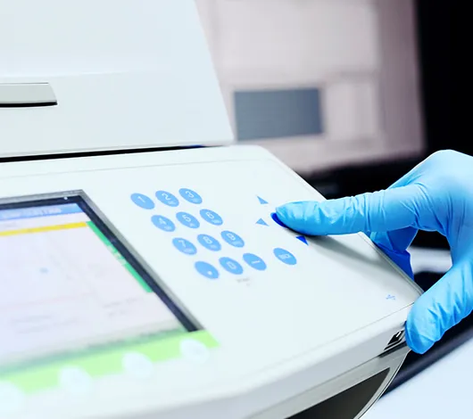 Finger pressing setting buttons on thermocycler for PCR, with NEBinspired logo