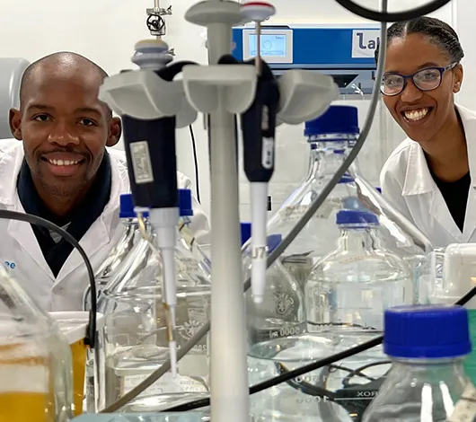 Photo of 2 lab scientists looking through shelving in lab setting