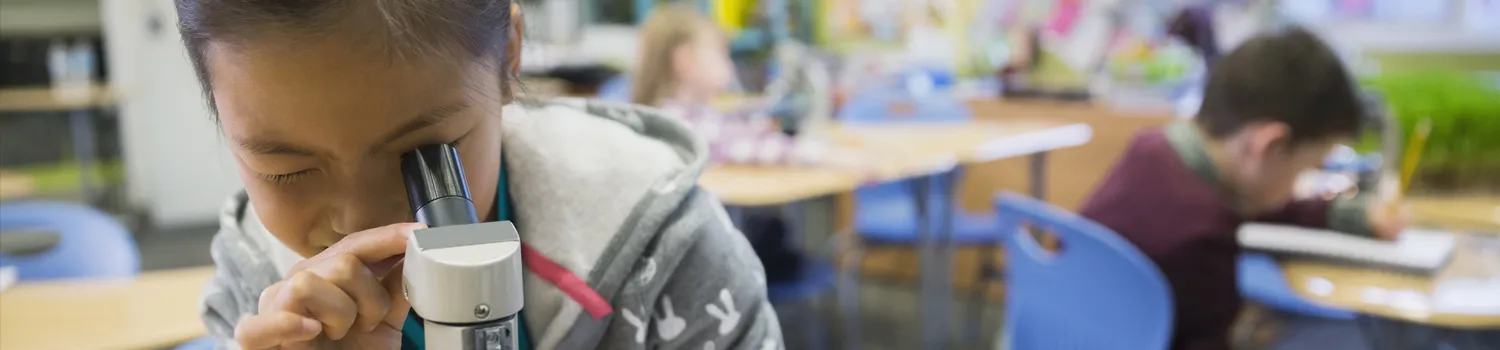 Elementary school girl looking though microscope in classroom